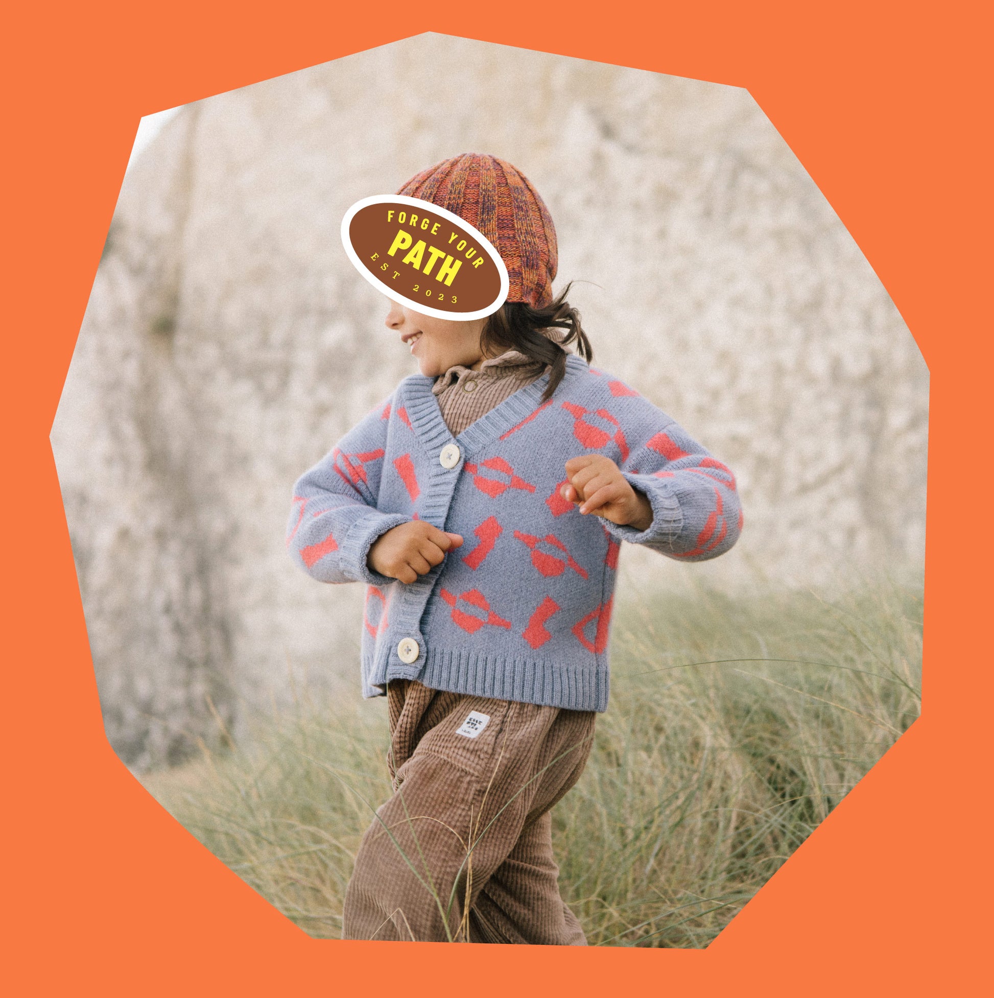 Child in wool cardigan in blue and coral jacquard, running on sand dunes.