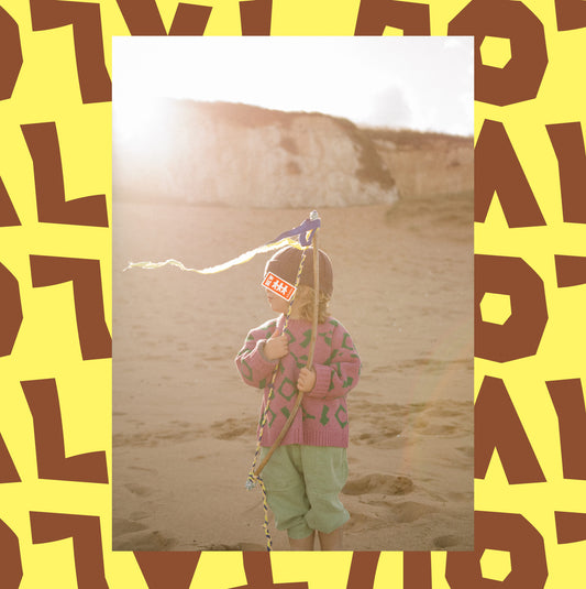 Child on beach wearing pink and green wool jaquard knit jumper.