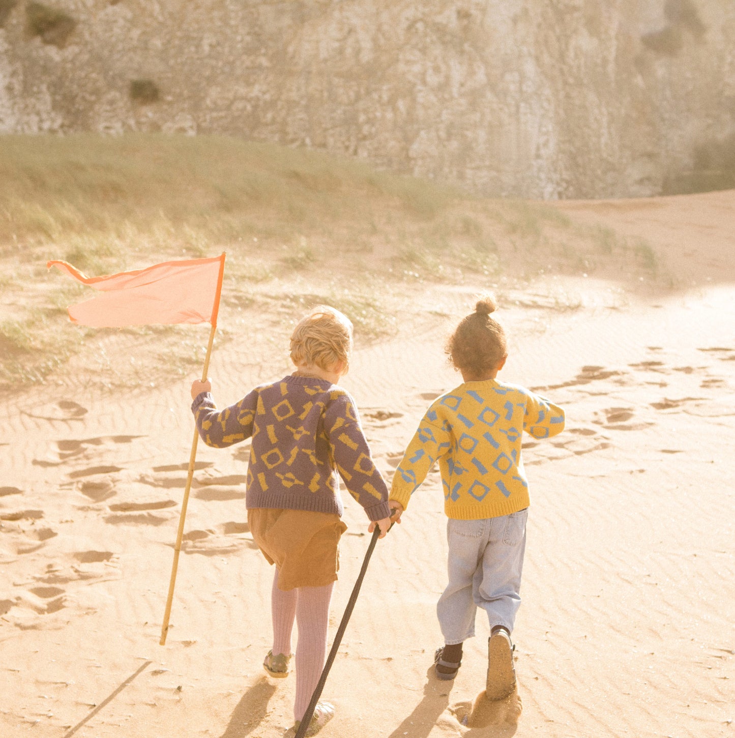 Children running up a sand dune wearing colourful wool knitwear.
