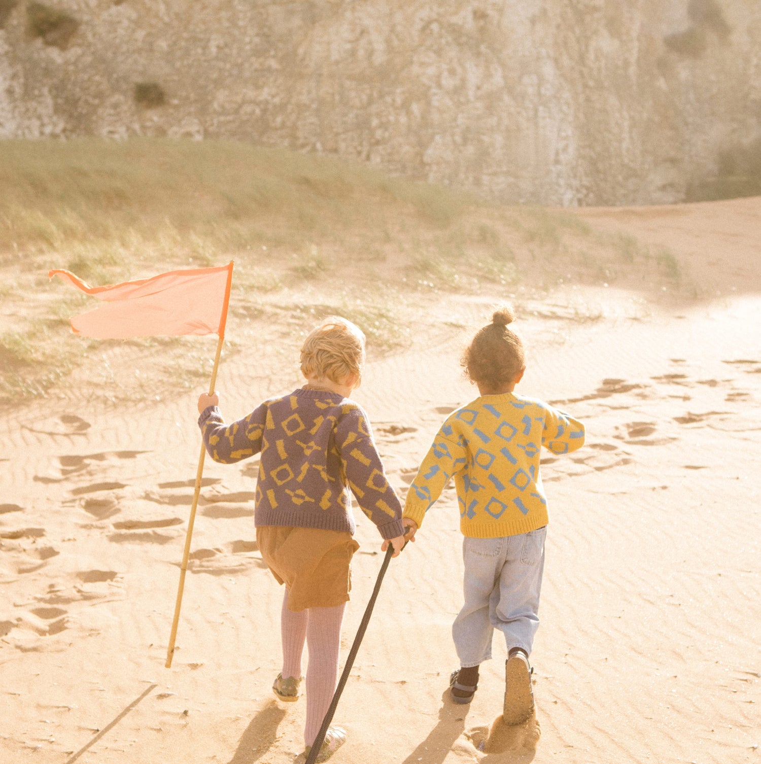 Children running up a sand dune wearing colourful wool knitwear.