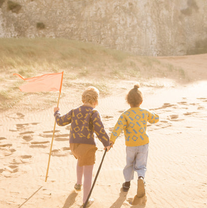 Children running up a sand dune wearing colourful wool knitwear.